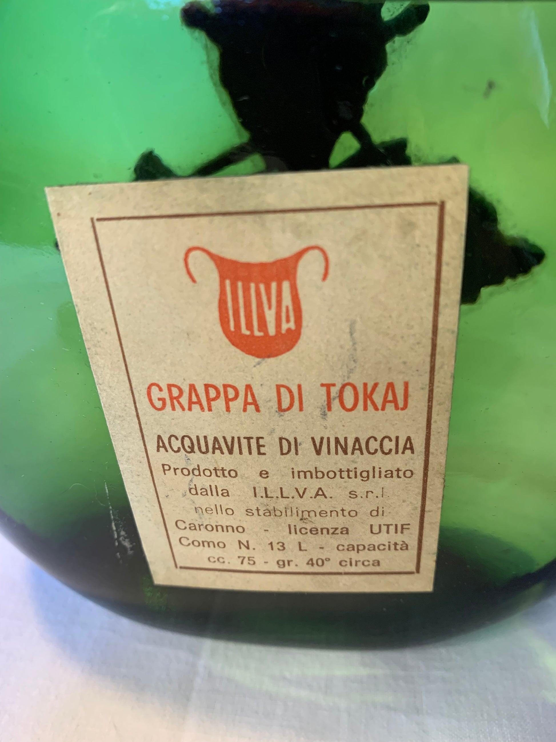 Vintage Tokai grappa bottle by I.L.L.V.A. with green glass, pewter neck, spout, and grapevine detail. Original label and seal intact – 1960s/70s.
